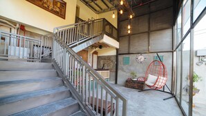Un escalier avec des rampes en métal mène à une mezzanine. Au rez-de-chaussée, on trouve un fauteuil en forme d’œuf de couleur rouge et une petite table sur laquelle est posée une plante.
