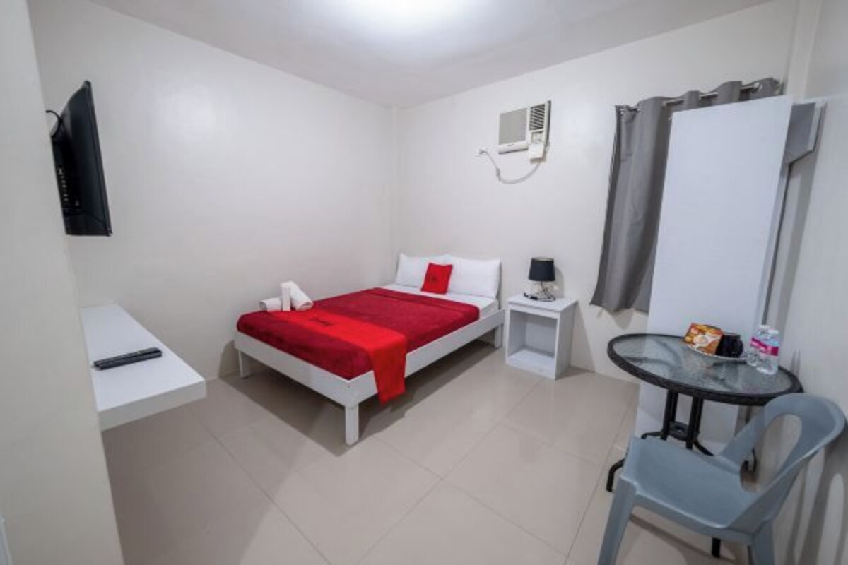 Een hotelkamer met een bed, nachtkastje, stoel en een tafeltje met een lamp.