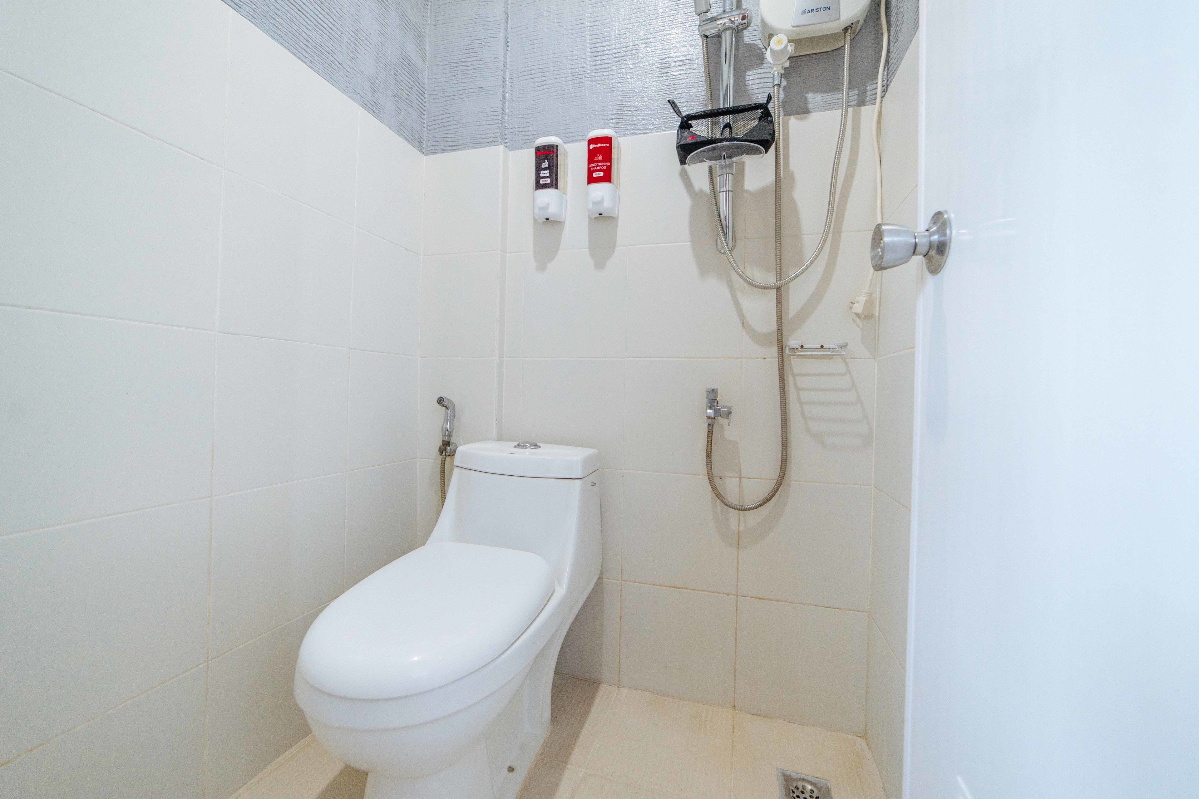 A small, white bathroom with a toilet, a shower, and two soap dispensers on the wall.