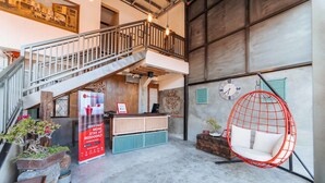 Un hall d’entrée spacieux avec un escalier, un comptoir d’accueil, un fauteuil rouge suspendu et une horloge au mur.