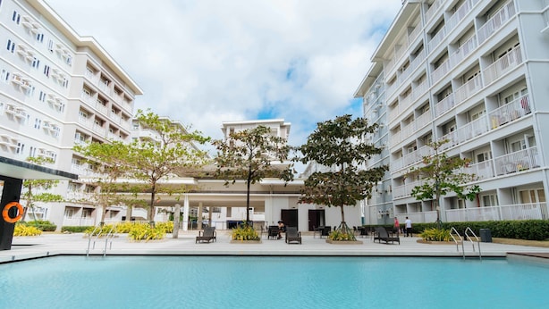 A swimming pool surrounded by modern buildings with balconies, outdoor seating, and greenery. - RedDoorz Premium @ SMDC Fairview (Quezon City)