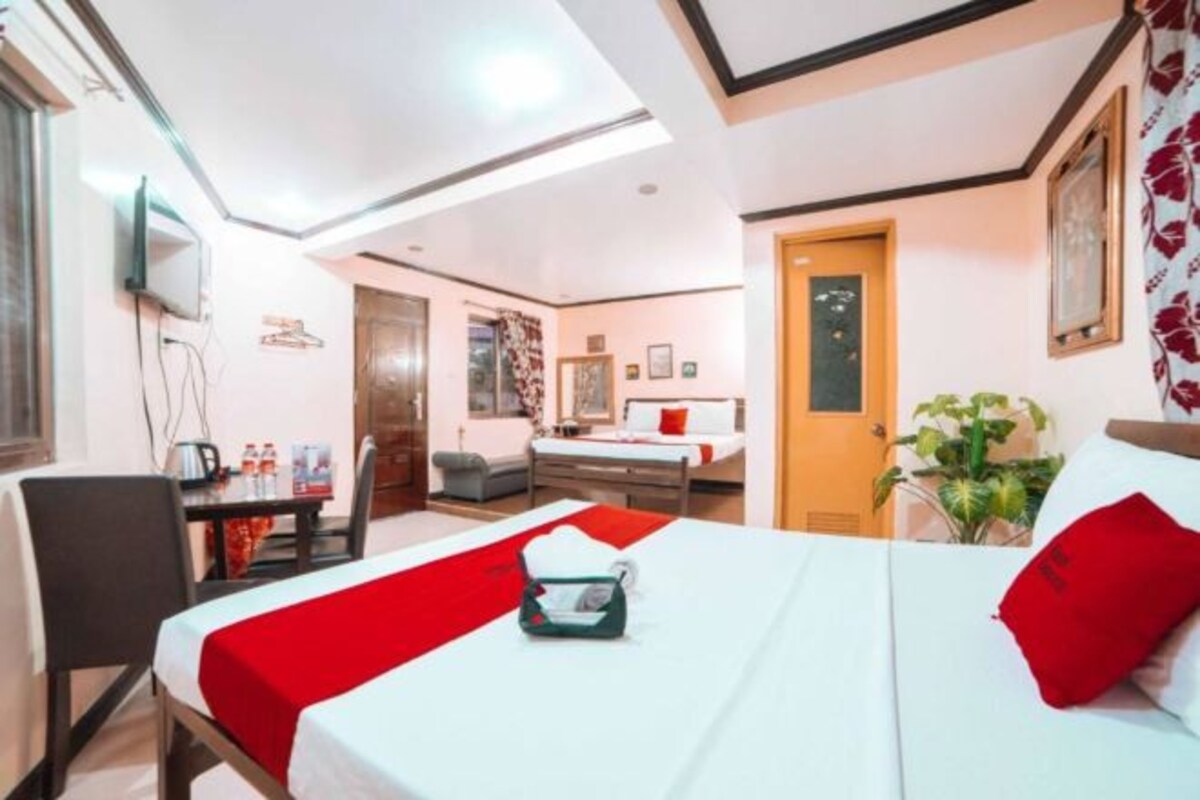 A hotel room with a bed, a desk, and a chair. There is a door leading to another room.