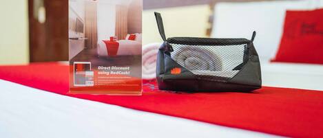 Un letrero promocional de RedDoorz y una bolsa de malla negra sobre una cama con una manta roja.