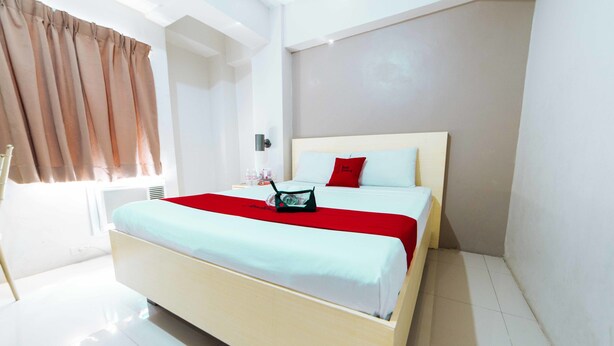 Una habitación de hotel moderna con una cama grande, un plaid rojo, una computadora portátil y una ventana con cortinas.