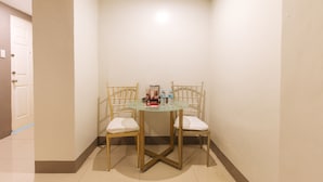 Habitación de esquina con una mesa redonda de cristal y dos sillas con cojines blancos. Hay una puerta a la izquierda y una pared a la derecha.