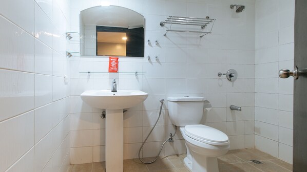A bathroom with white tiles, a sink, a toilet, a glass shelf, and a showerhead.