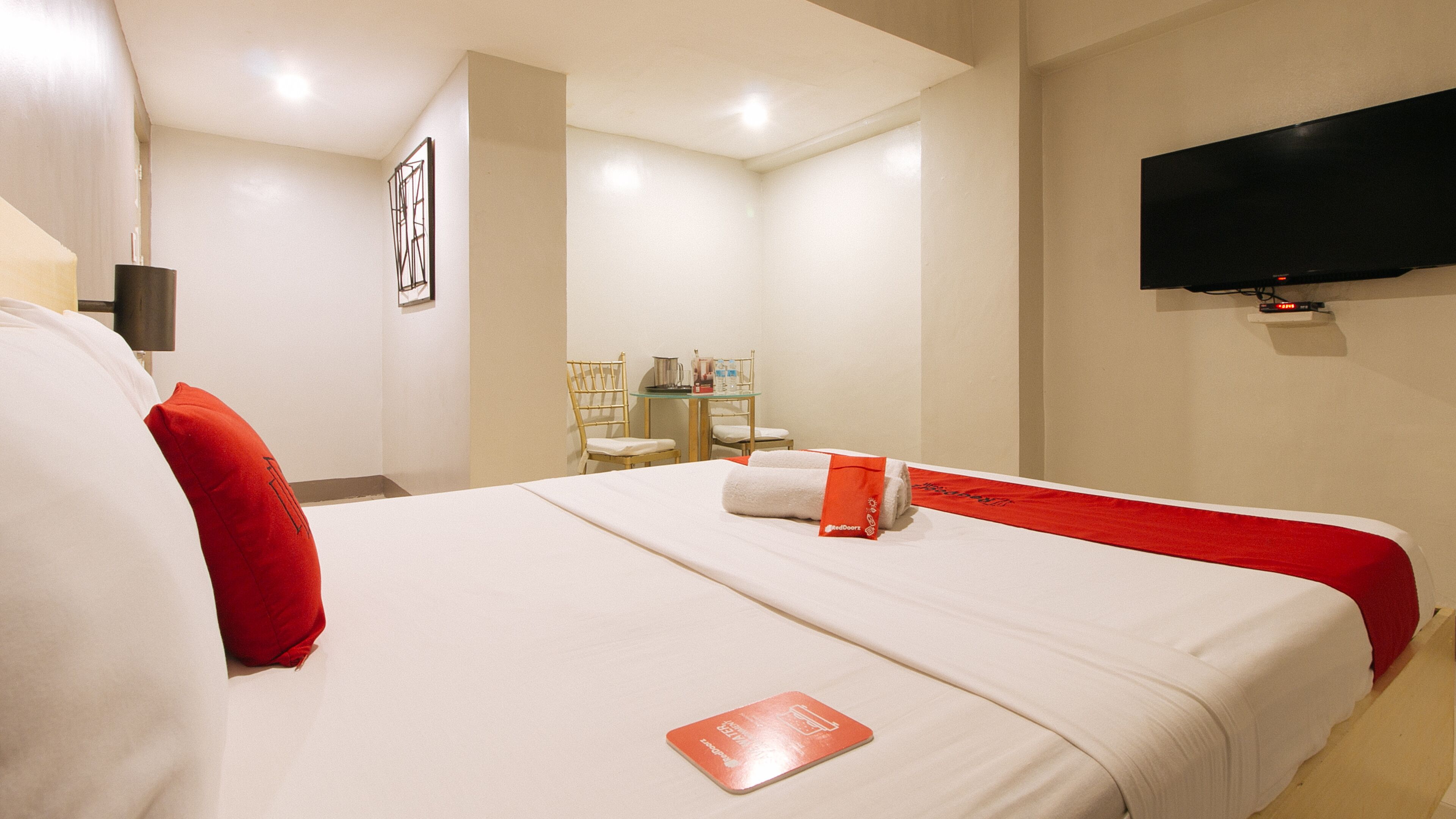 A hotel room with a bed, a TV mounted on the wall, and a small table with chairs.