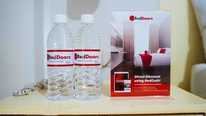 Dos botellas de agua RedDoorz y un folleto promocional de RedDoorz sobre una mesita de noche.