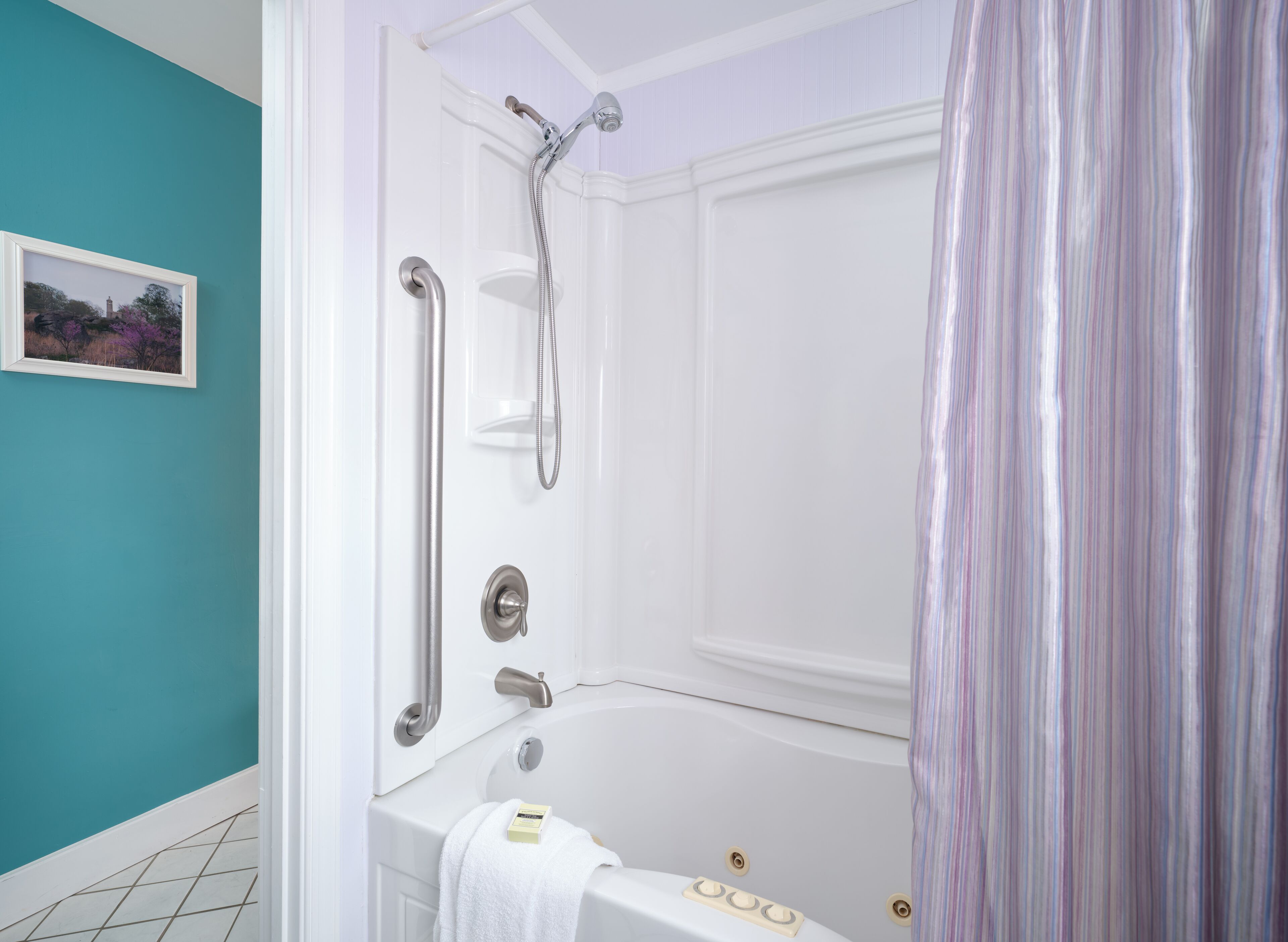 Un baño con bañera, ducha e inodoro. Hay una toalla colgada en la pared y un marco de fotos.