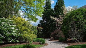 A garden pathway with various plants and trees, a hanging flower pot, and a stone walkway. - Keystone Inn Bed and Breakfast (Gettysburg)
