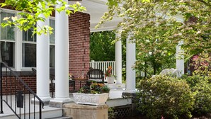 A covered porch with white columns, a brick wall, and a seating area with a table and chairs. - Keystone Inn Bed and Breakfast (Gettysburg)