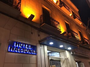 The exterior of Hotel Nacional with illuminated signage and a stone facade. - Hotel Nacional (Melilla)
