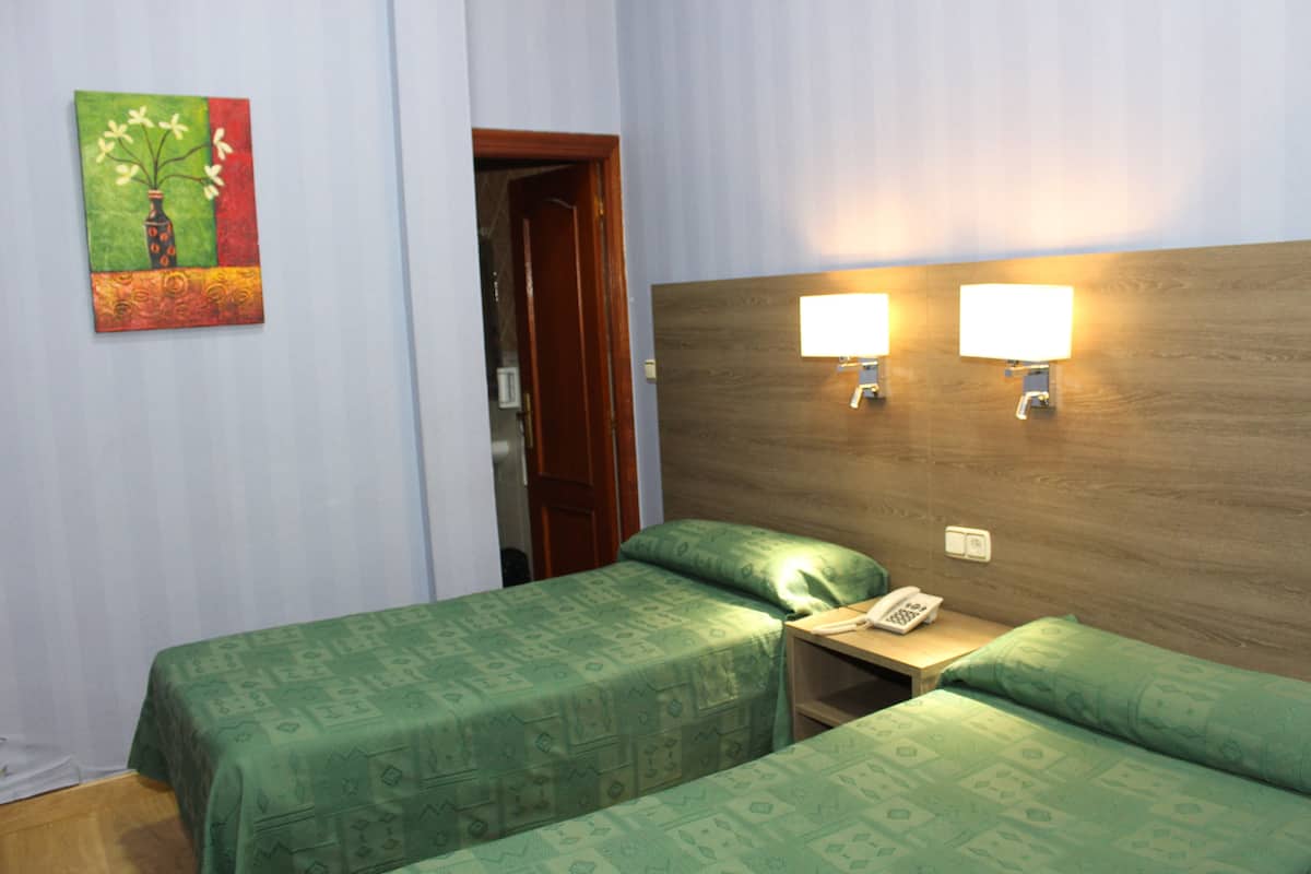 A hotel room with two single beds, a wooden headboard, bedside lamps, a telephone, and a painting on the wall.