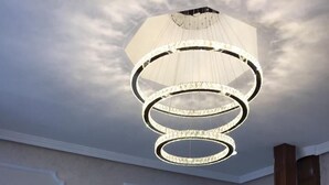 A lobby with a modern chandelier, a clock, and a wooden panel wall. - Hotel Nacional (Melilla)