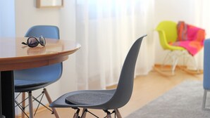 Een kamer met een houten tafel, een zonnebril, een grijze stoel en een kleurrijke stoel op de achtergrond.