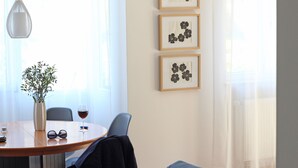 Een eethoek met een ronde tafel, stoelen, een vaas met planten, een wijnglas en lijstwerken aan de muur.