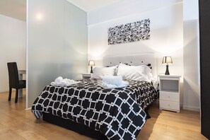 A modern hotel room with a black and white patterned bedspread, two bedside tables with lamps, a wall art piece, and a wooden floor.