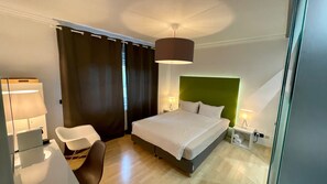 A hotel room with a bed, two bedside tables with lamps, a chair, and a large window with curtains. - smart&beautiful Deluxe (Nordkirchen)