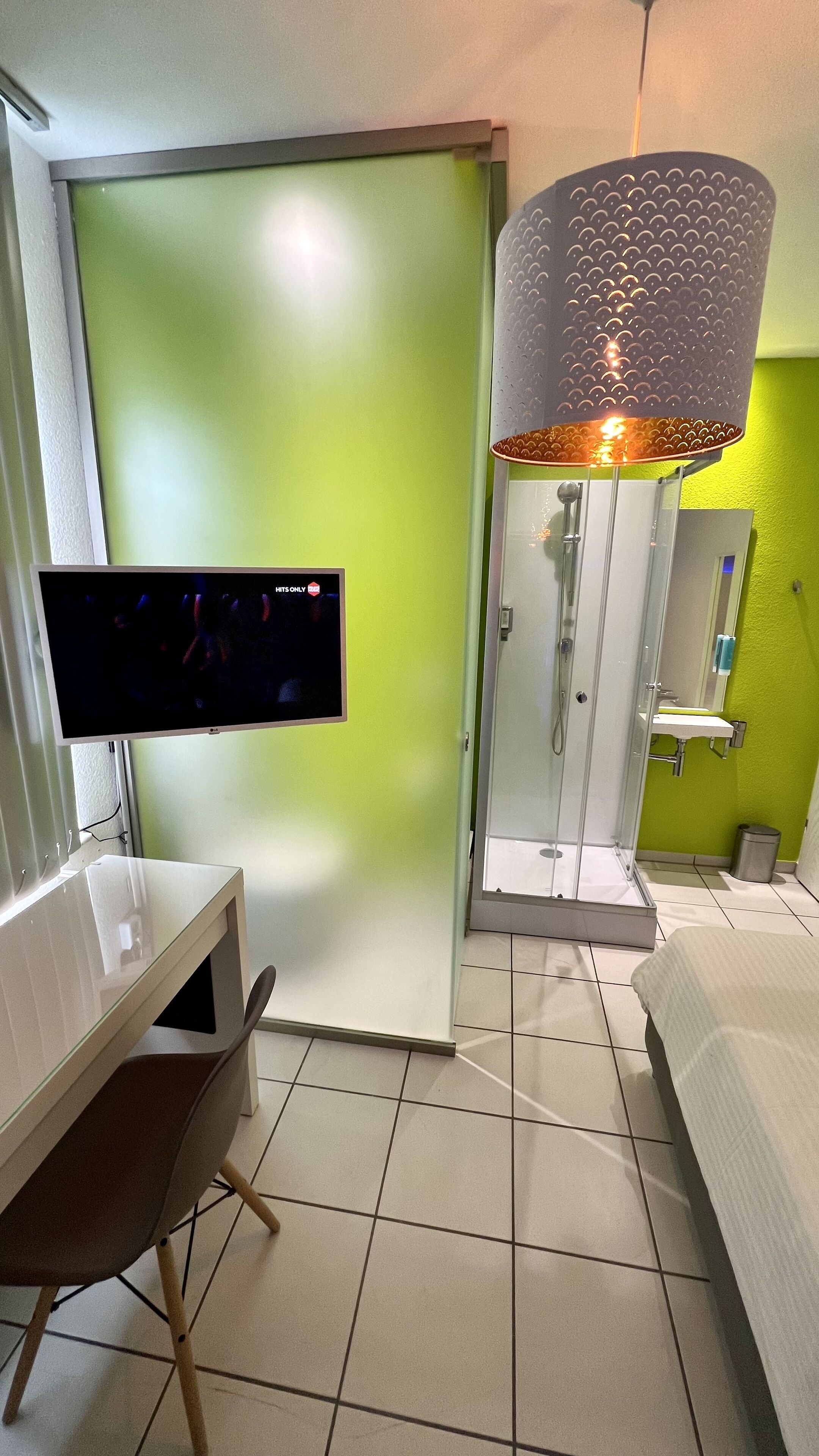 Ett hotellrum med en grön vägg, en platt-TV, en dusch, ett handfat och en säng.