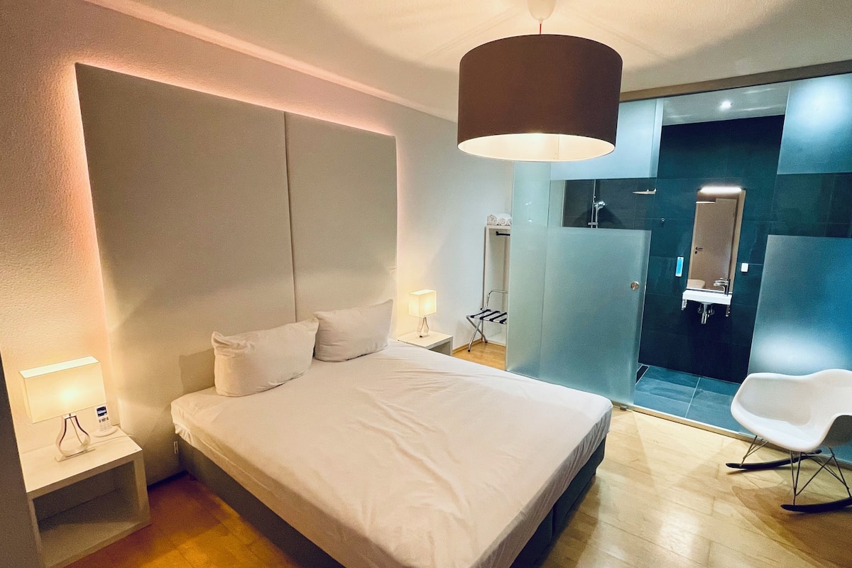 Una habitación de hotel moderna con una cama grande, lámparas de noche, un espejo y una zona de estar.