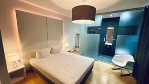 A modern hotel room with a large bed, bedside lamps, a mirror, and a seating area. - smart&beautiful Deluxe (Nordkirchen)