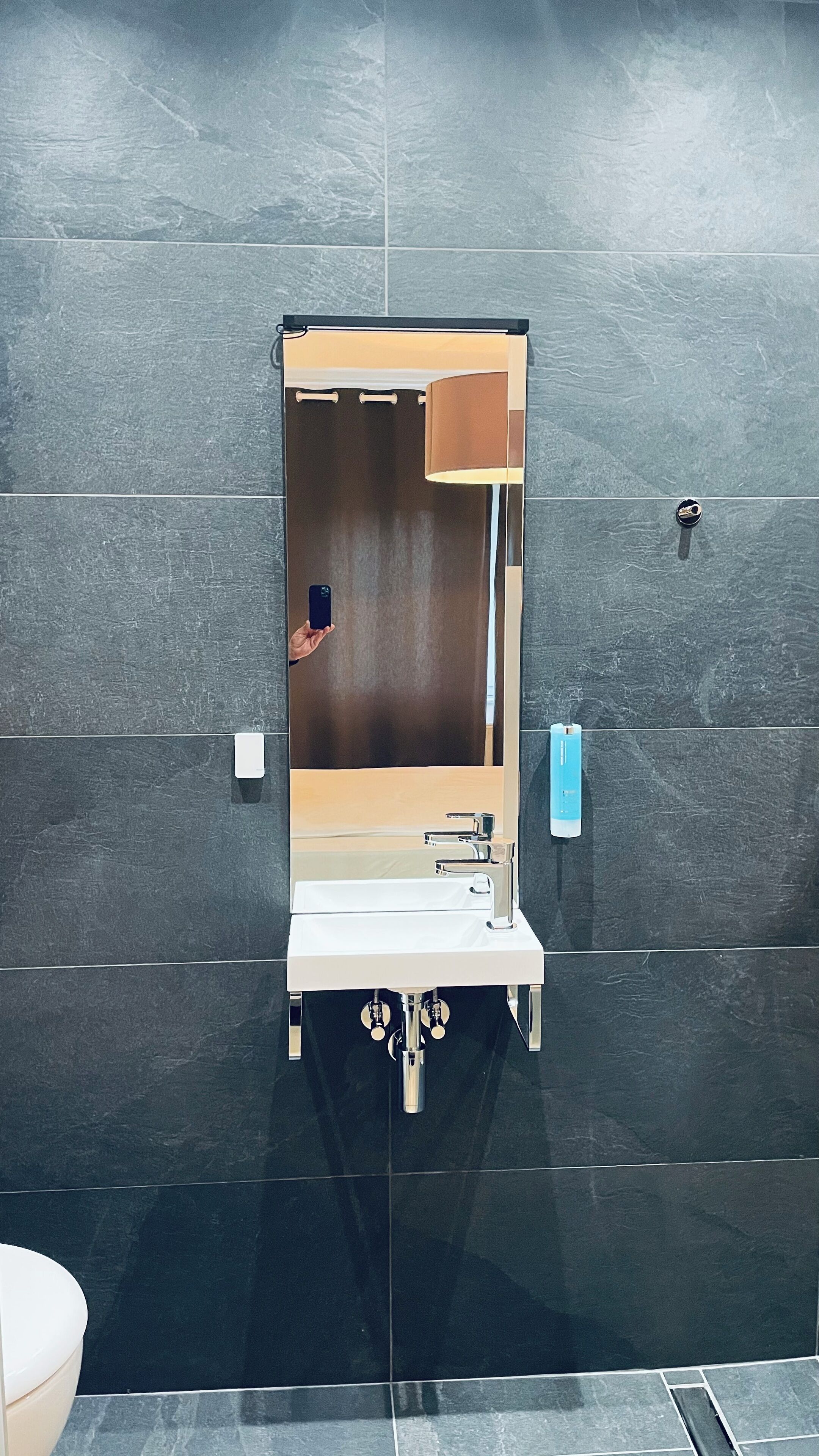 Une salle de bain moderne avec un grand miroir, un lavabo et un distributeur de serviettes.
