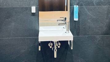 Une salle de bain moderne avec un grand miroir, un lavabo et un distributeur de serviettes.