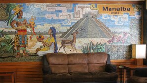 A hotel lobby with a large mural depicting ancient Mayan culture, a brown leather sofa, and a wooden bench. - Hotel Manalba (Mexico City)