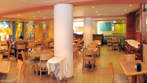 A restaurant with multiple tables and chairs, a large pillar, and colorful wall art. - Hotel Manalba (Mexico City)