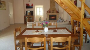 A dining area with a wooden table and chairs, a fireplace, and a staircase. - Rodies Cottage (Kefalonia)