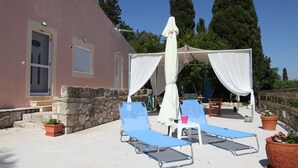 A sunlit outdoor seating area with two blue lounge chairs, a white umbrella, and potted plants. - Rodies Cottage (Kefalonia)
