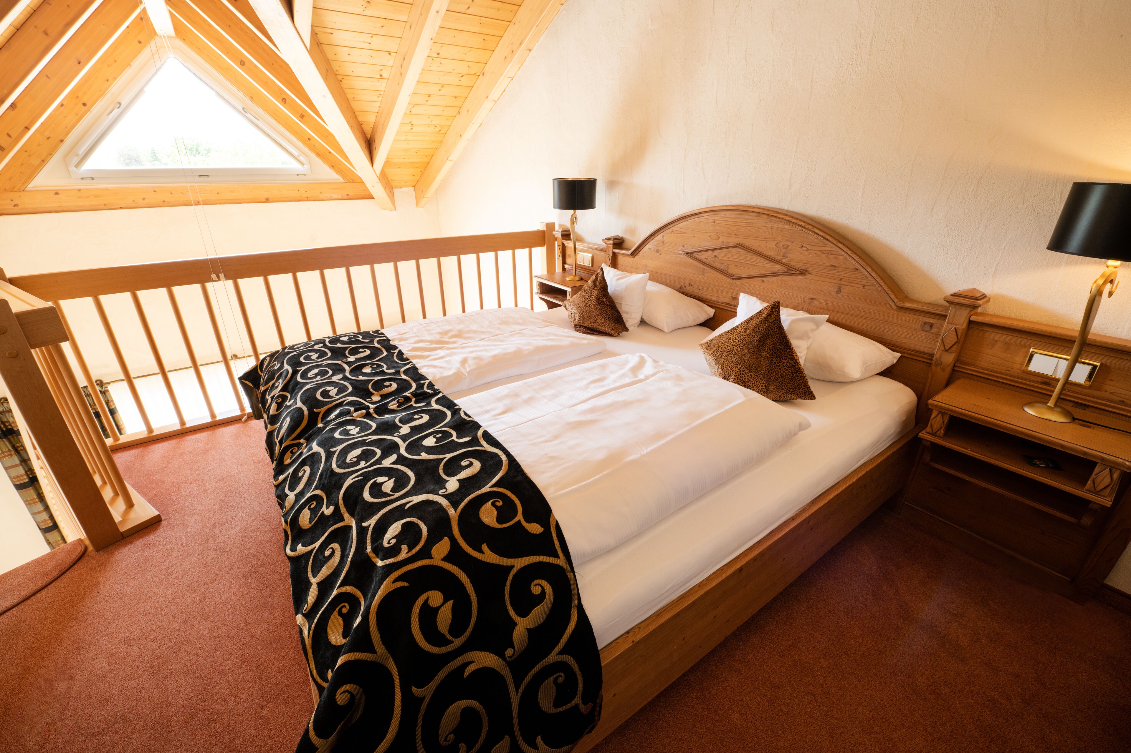 A bedroom with a wooden bed, a skylight, a nightstand with a lamp, and a wooden railing.
