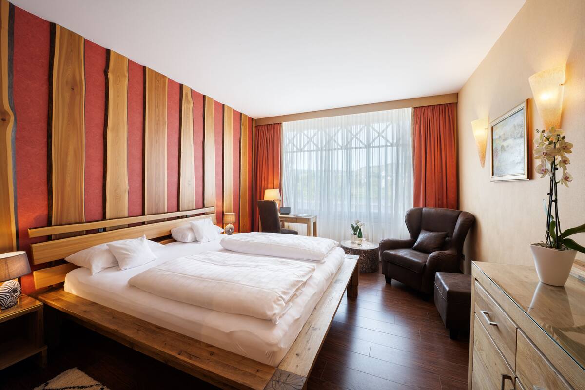 A hotel room with a large bed, a desk, a chair, and a potted plant.