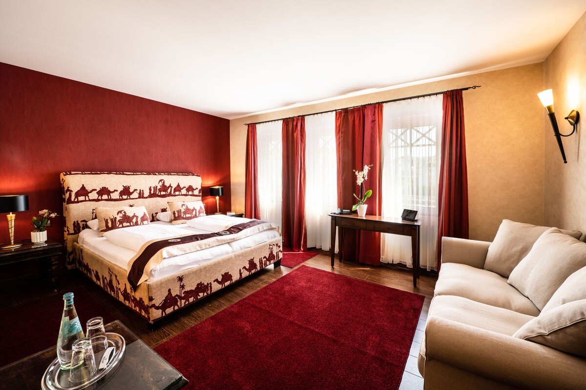 Une chambre d’hôtel avec un grand lit, un canapé, une petite table et une moquette rouge.
