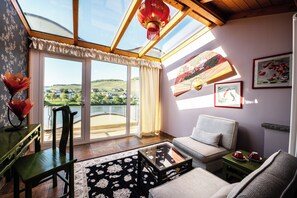 A room with a large glass door leading to a balcony, a sofa, a table, and a chair. - Wellness- & Genusshotel Weisser Bär (Muelheim)