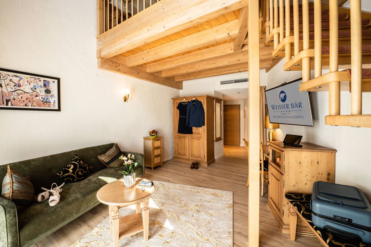 A cozy hotel room with a wooden staircase, a green sofa, a small table, and a blue suitcase.