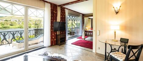 A spacious room with a large glass door leading to a balcony, a flat-screen TV, a glass coffee table, and a leather sofa.