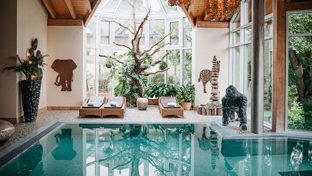 A pool area with lounge chairs, a large tree, and decorative sculptures. - Wellness- & Genusshotel Weisser Bär (Muelheim)