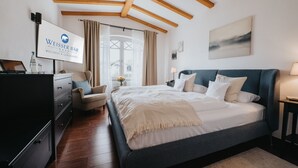 A bedroom with a bed, a dresser, a chair, a desk, and a TV displaying the hotel name. - Wellness- & Genusshotel Weisser Bär (Muelheim)