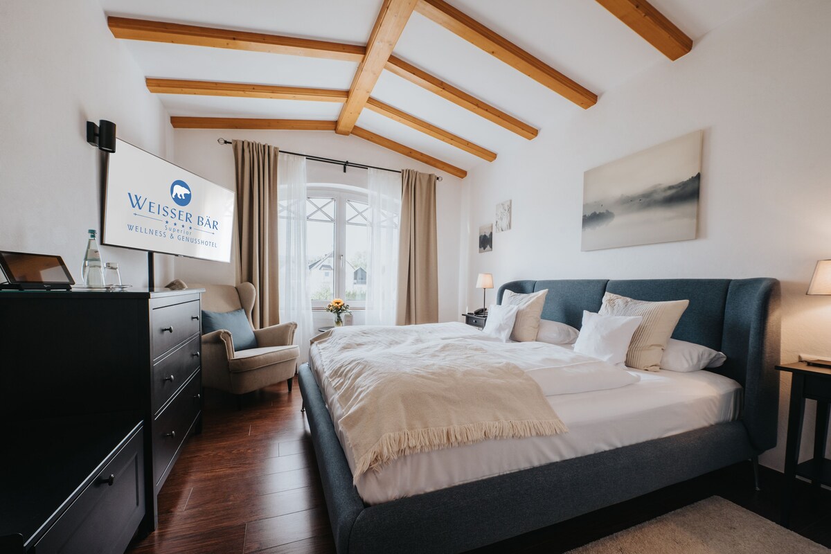 Une chambre à coucher comprenant un lit, une commode, une chaise, un bureau et un téléviseur affichant le nom de l’hôtel.