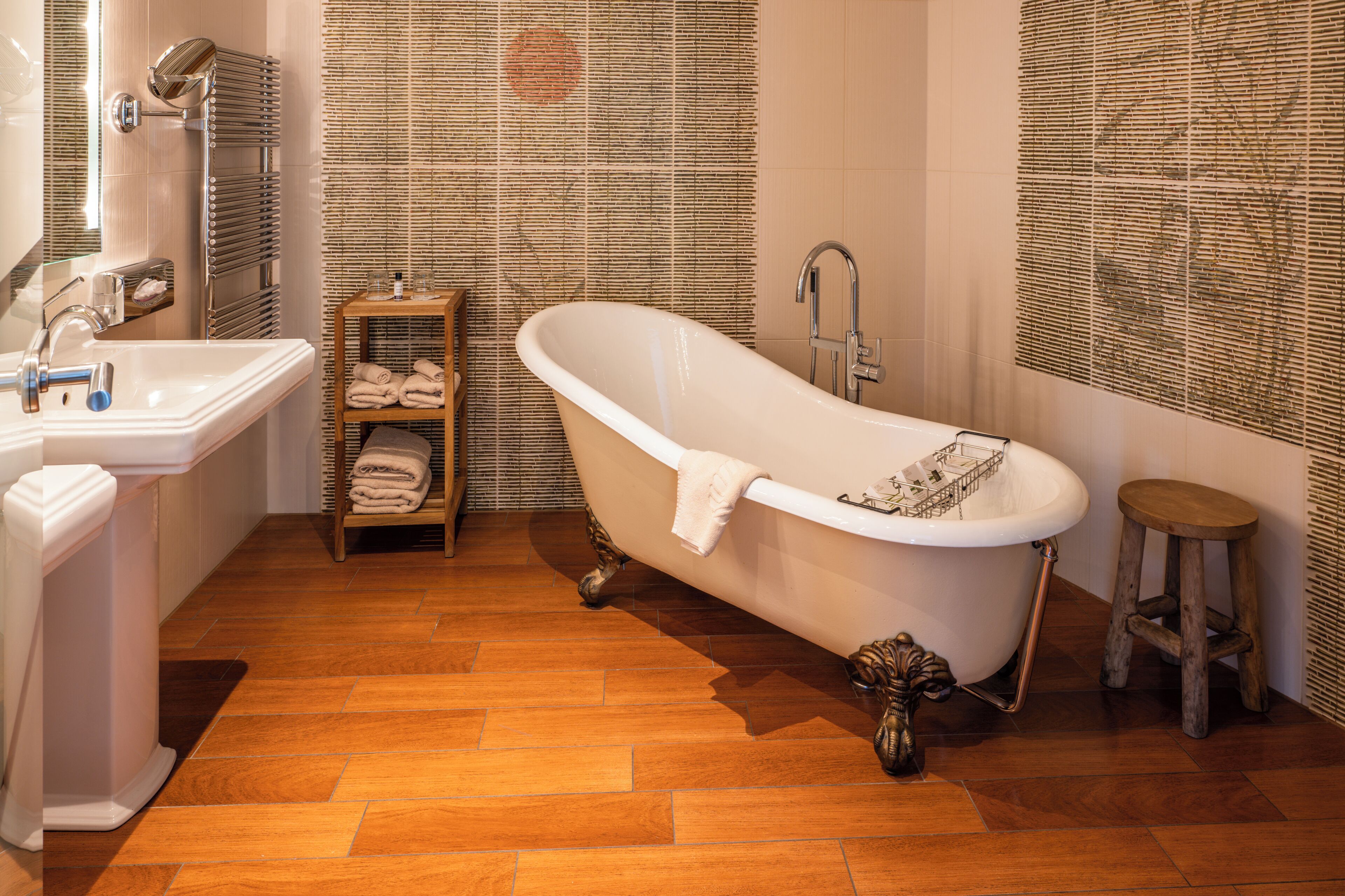 A bathroom with a freestanding bathtub, a sink, and a wooden shelf with towels.