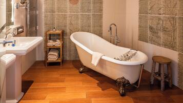 Un baño con una bañera independiente, un lavabo y un estante de madera con toallas.