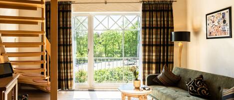 A living room with a sofa, a small table, a lamp, and a view through a glass door to the outdoors.