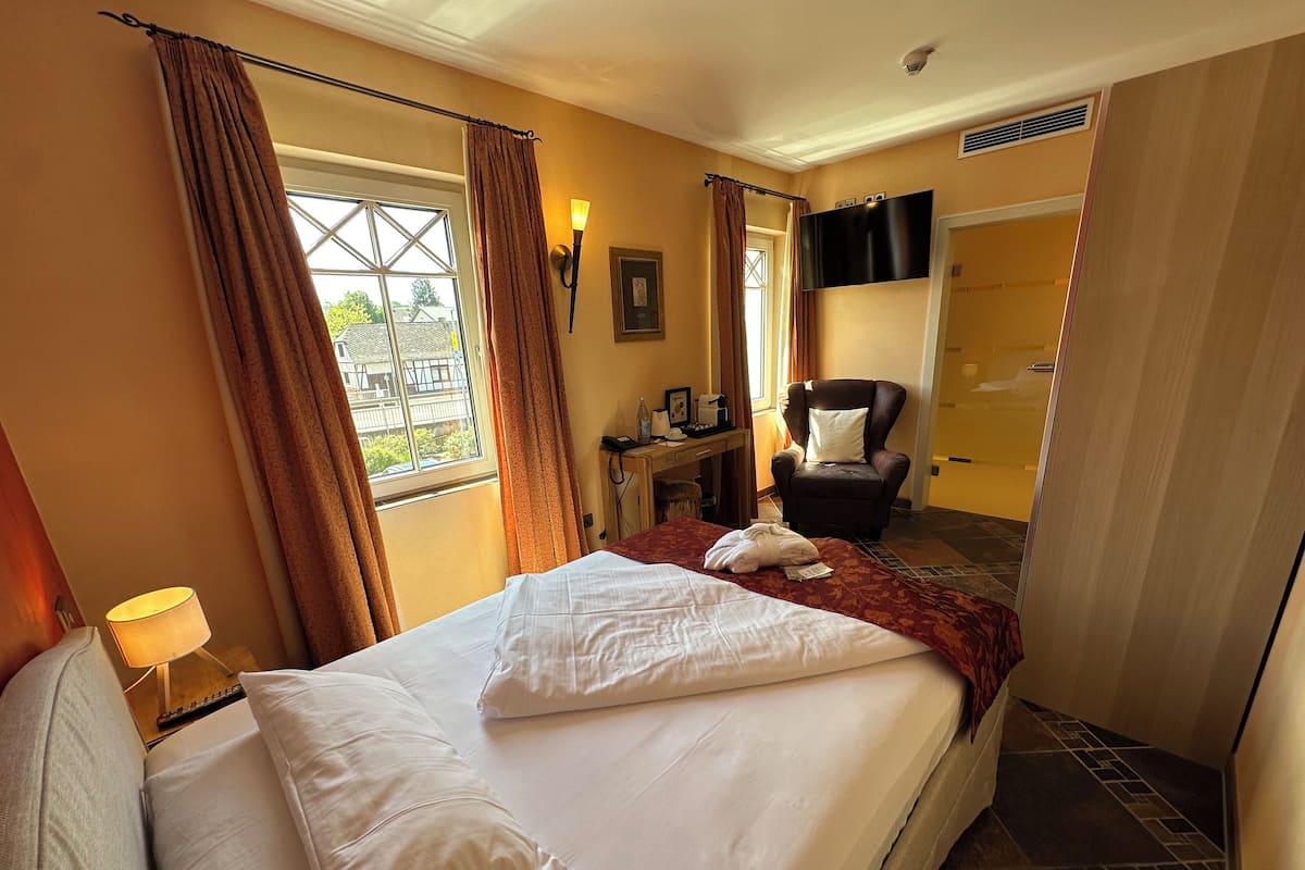 A hotel room with a large bed, a chair, a desk with a lamp, and a view of the outside.
