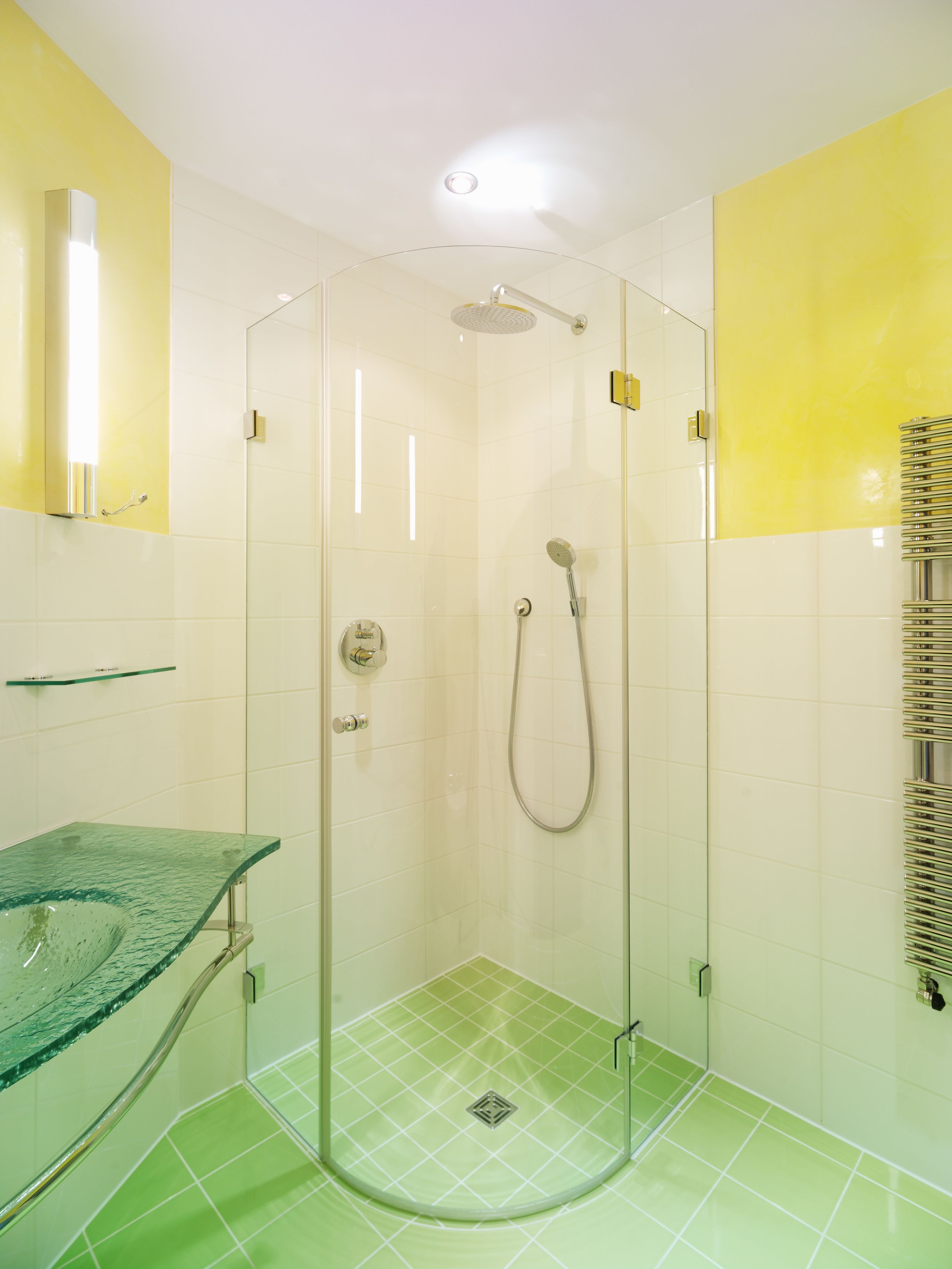 A glass-enclosed shower with a handheld showerhead and a wall-mounted faucet.