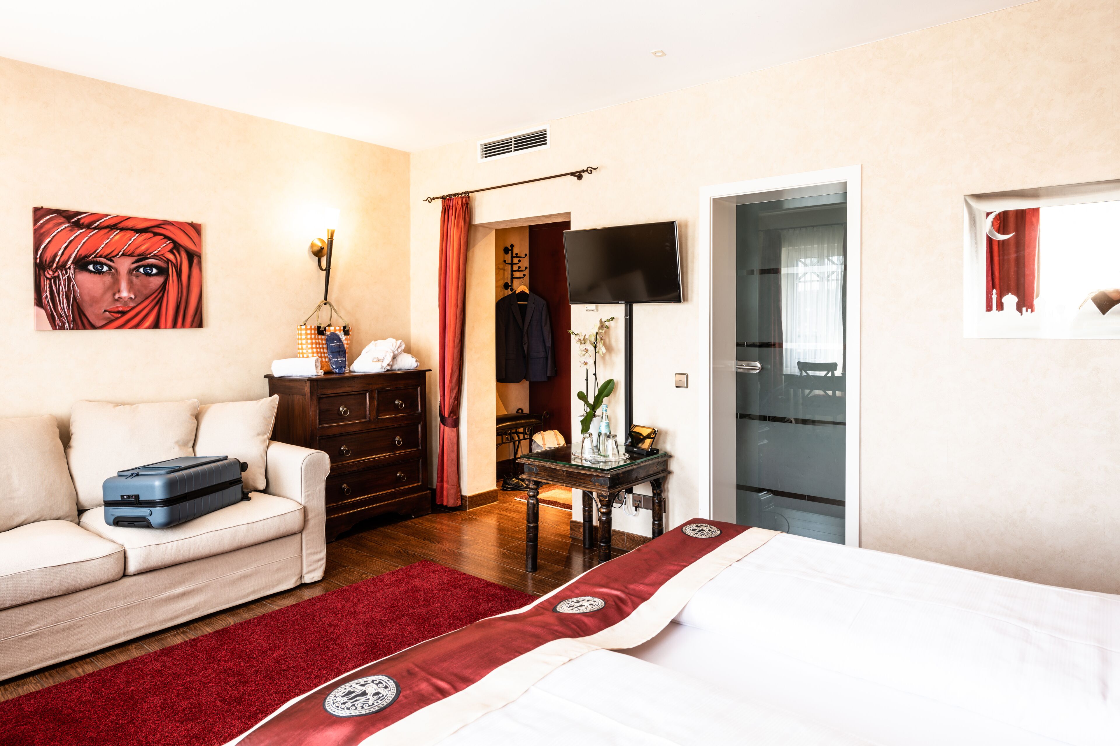 Ein Hotelzimmer mit Bett, Sofa, Kommode, Fernseher und einem Bild an der Wand.