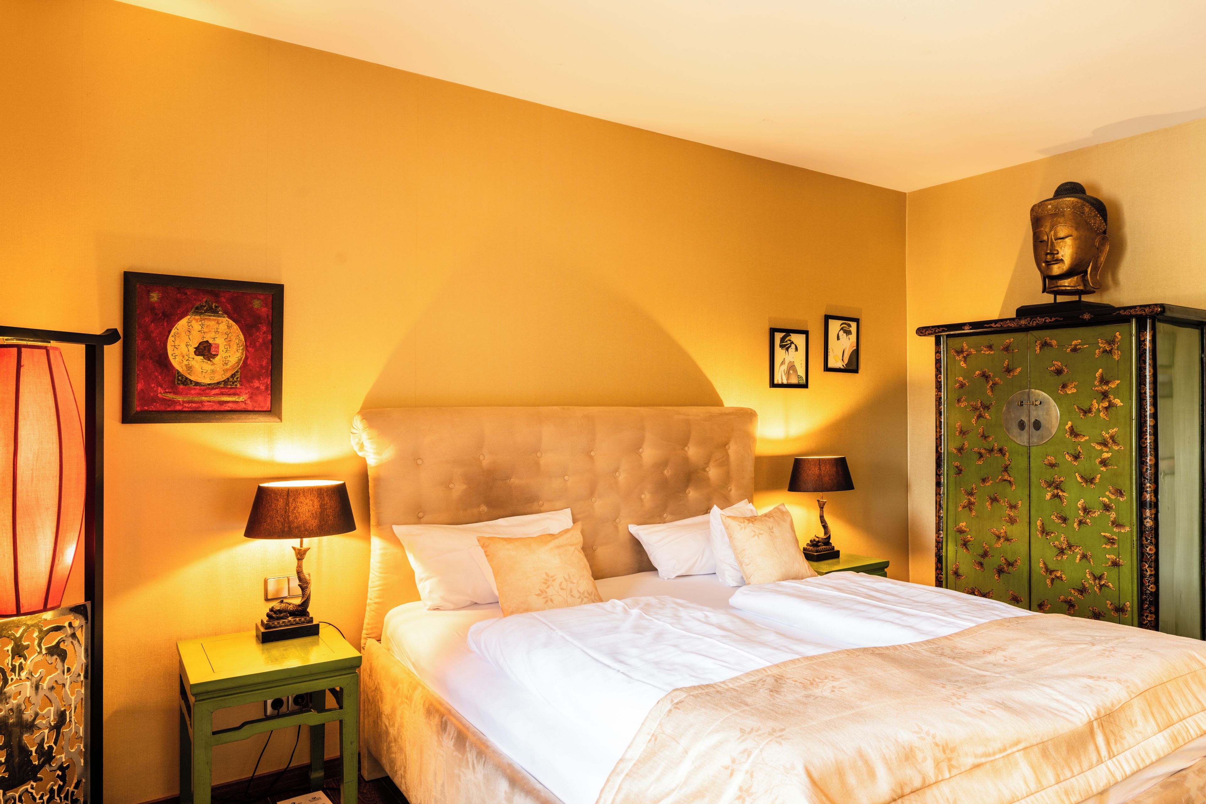 A hotel room with a large bed, two bedside tables, a green cabinet, and artwork on the walls.