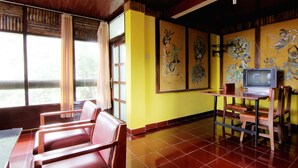 A room with wooden ceiling, yellow walls, a TV on a table, and a window with curtains. - Vogels Hostel (Pakem)
