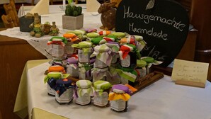 Uma mesa com potes de marmelada, um letreiro com a inscrição 'Hausgemachte Marmelade' e uma lista de preços.