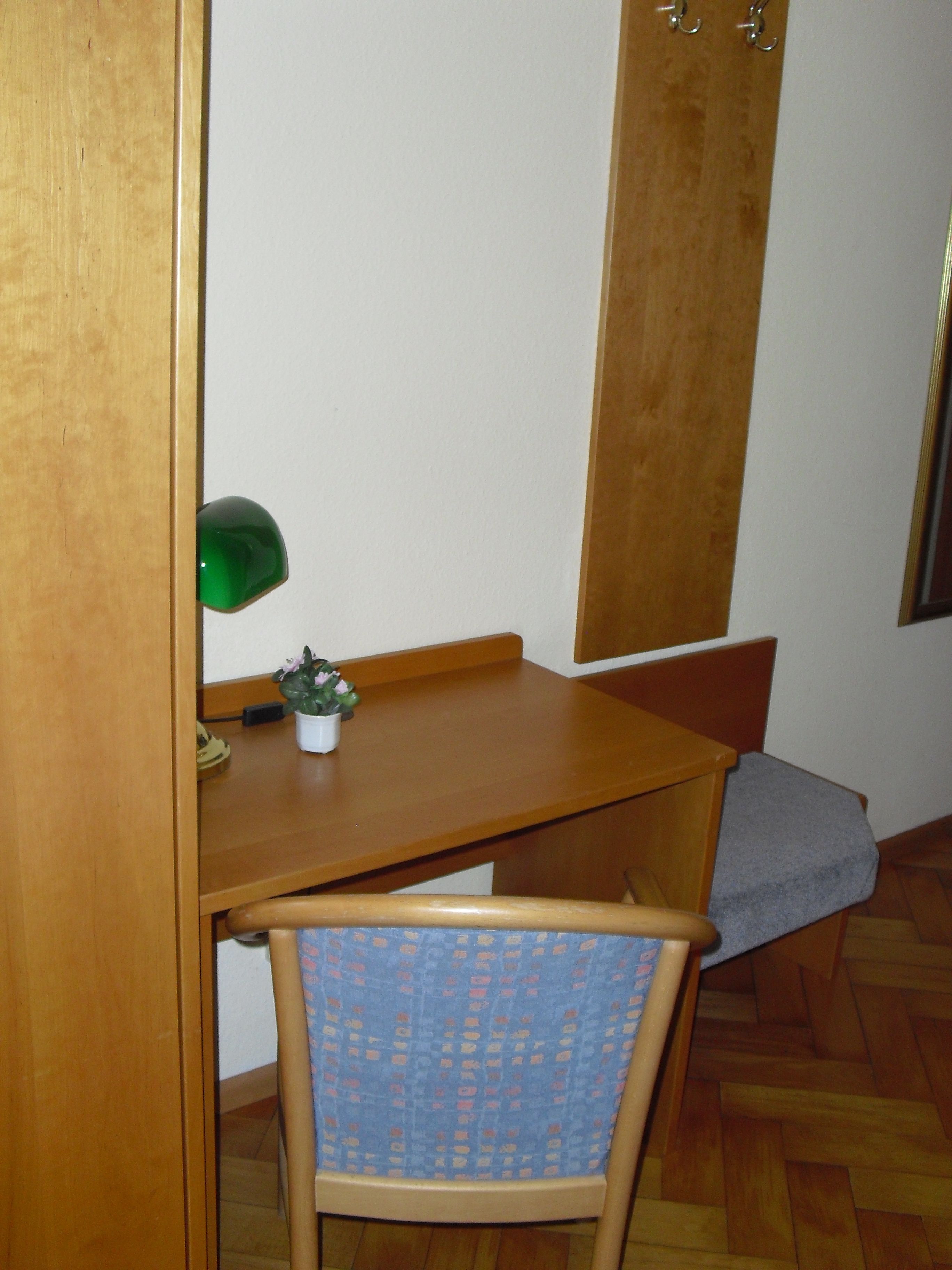 Ett litet skrivbord i trä med en stol, en grön lampa och en liten krukväxt.